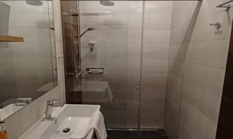 A modern bathroom with a glass shower partition. The amenities include a sink and an elegant wooden shelf.