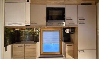 A modern kitchen with wooden fronts and a stove. The windows offer a view of nature and the room feels bright and inviting.