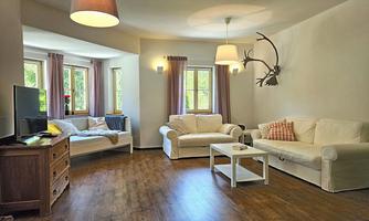 A bright living room with large windows and modern furniture. There is a comfortable sofa, a coffee table, and a television.