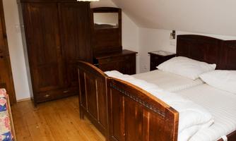 A cozy bedroom with two beds and a wooden wardrobe. The floor is made of wood and the furniture has a classic style.
