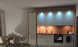 A modern kitchen with a cooking field, refrigerator, and stylish skylights. A dining table with chairs is nearby.