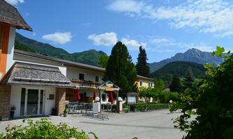 A beautiful inn in a picturesque mountain landscape.  
Surrounded by trees and mountains under a clear blue sky.
