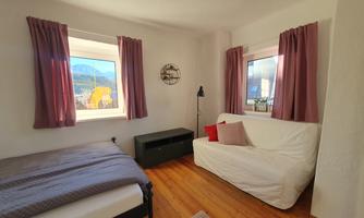 A cozy room with two windows, a bed, and a sofa. The walls are light, and the curtains are in soft colors.