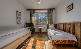 A modern room with two single beds and a television. Large windows let in plenty of light and offer a view of the outdoors.