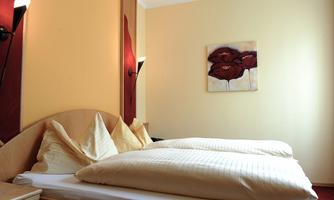 A cozy bedroom with a large bed and beige pillows. On the wall hangs a picture with red flowers.