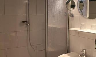 A bathroom with a shower and a sink. The walls are decorated with white tiles and a green accent.