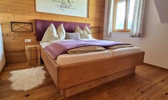 A cozy bedroom with wooden flooring and wooden walls. The double bed has a purple blanket and comfortable pillows.