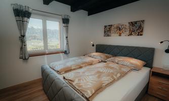 A modern bedroom with a cozy bed and large windows. The view of the countryside brings light into the room.