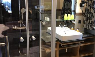 A modern bathroom with a glass shower and a stylish sink. The decor is in warm wooden tones, and there are decorative curtains.