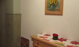 An entrance area with a wooden table and a red flower-like decoration. On the wall hangs a picture of sunflowers.
