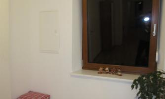 A bright room with a window and a small sitting area. On the windowsill are some decorative elements and a plant.