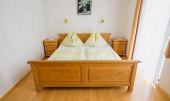 A cozy bedroom with a wooden bed and two nightstands. The bedding is in soft shades of yellow, and a picture hangs on the wall.