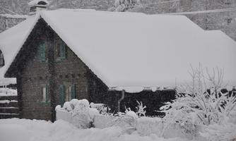 A snow-covered house in a wintry landscape. The surroundings are quiet, and the trees are also covered with snow.