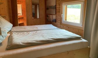 A cozy bedroom with wood decor and a large window. The bed is made and invites you to relax.