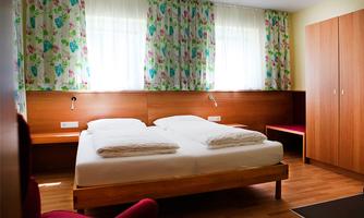 A bright bedroom with a double bed and floral curtains. The floor is made of wood and there is a cozy seating area.