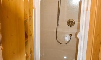 A bright shower in a bathroom with wooden details. Next to the shower stands a wooden shelf cabinet.