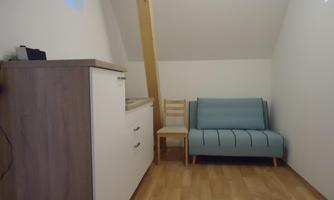 A small room with a blue sofa and a chair. Against the wall are a white chest of drawers and a window.