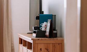 A cozy room with a television on a wooden cabinet. On it are a coffee machine and informational materials.