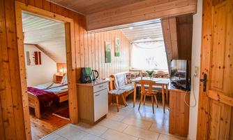 A cozy apartment with wood paneling and a small dining area. In the background, the bedroom is visible.