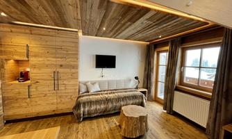 A modern room with wood decor and a cozy atmosphere. It features a bed, a television, and large windows with a view outside.