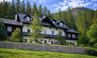 A charming house, surrounded by trees and a green meadow. In the background, gentle hills and a blue sky can be seen.