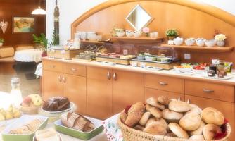 An inviting breakfast buffet with various rolls, cakes, and spreads. The room has a bright and friendly atmosphere.