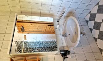 A bathroom with tiled walls, a round sink, and a large mirror. In the background, there is a wooden terrace door and a towel rack.