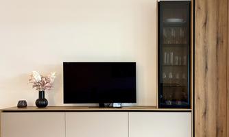 A modern living room with a large television on a low piece of furniture. Next to the television is a vase with flowers and a glass door cabinet.