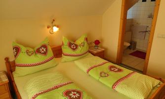 A cozy bedroom with two beds and colorful pillows. In the background, you can see a bathroom.