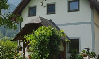A beautiful house with a landscaped front yard. It is surrounded by trees and mountains.
