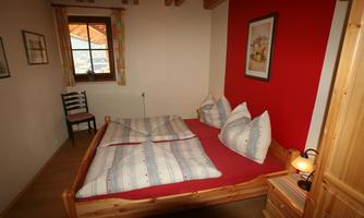 A cozy bedroom with a large bed and decorative pillows. The walls are light, and a red accent adds warmth to the space.