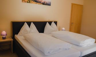 A cozy bedroom with a large double bed and white bedding. Pictures of mountain landscapes hang on the walls, and there is gentle light from bedside lamps.