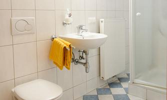 A modern bathroom with white tiles and a sink. Towels in warm yellow hang decoratively next to the toilet.