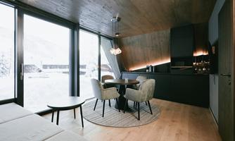 A modern kitchen with a dining area and large windows. The room is bright and inviting, with a cozy wooden floor.