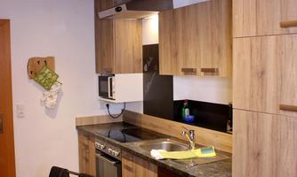 A modern kitchen with wooden cabinets and a large table. The equipment includes a stove, a sink, and several kitchen appliances.
