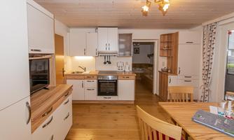 A modern kitchen with white cabinets and wooden details. The space is bright and open, featuring a wooden dining table.