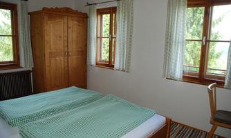 A cozy bedroom with a double bed and checkered blankets. Large windows let in plenty of light and offer a view of the green surroundings.