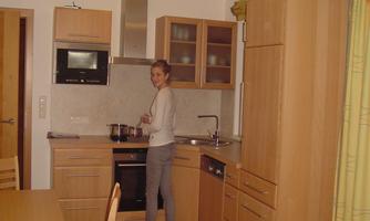A modern wooden kitchen with a cooking area and elegant cabinets. A person is standing at the stove preparing something.