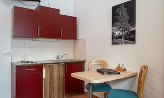 A small kitchenette in a modern room with red cabinets and a table with chairs. A black-and-white photo hangs on the wall.