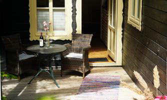 A cozy outdoor area with two chairs and a small table. On the table is a bottle of wine, and the surroundings appear inviting and calm.