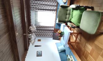 A cozy living room with blue seating and a green armchair. There is a table with flowers and a window that lets in daylight.