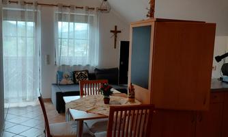 A cozy apartment with a dining area and modern furniture. The large windows provide plenty of daylight.
