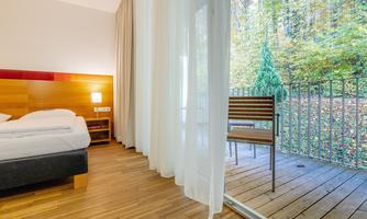 A modern room with a large window and a balcony. The view of the green surroundings creates a pleasant atmosphere.