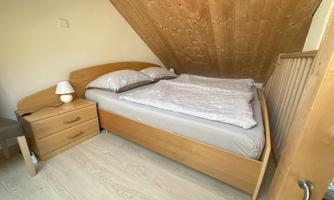 A cozy bedroom with a double bed and wooden decor. Next to the bed is a nightstand with a lamp.