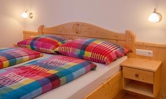 A comfortable bed with colorful bedding and two nightstands. The walls are light, and there is soft light from the wall lamps.