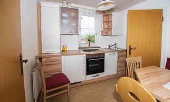 A modern kitchen with wooden and white cabinets. A dining table with chairs and a window with natural light can also be seen.