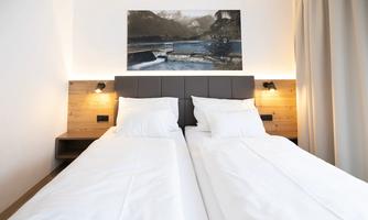 A modern bedroom with two single beds and a wooden panel headboard. Above the bed hangs a large painting of a landscape.