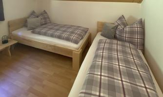 A cozy guest room with two single beds and checkered bedcovers. The floor is made of wood and the walls are light and simply designed.
