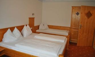 A cozy room with two beds and warm wooden furniture. The walls are painted in neutral colors, and a door leads outside.