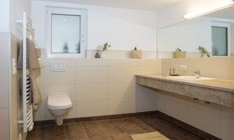 A modern bathroom with bright tiles and a large mirror. The facilities include a toilet, a sink, and towel holders.